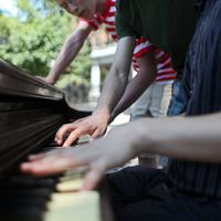 Three high school students playing a piano in Abe Lowenthal park in lower East Side in Manhattan waiting for a concert to begin on Make Music New York Day