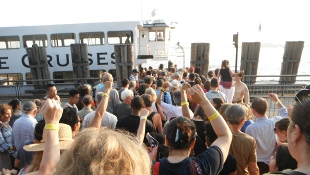 Audience members file onto the ferry that takes them to Governor's Island, yellow wristbands in the air.