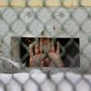A detainee shields his face as he peers out through the so-called 'bean hole,' which is used to pass food and other items into detainee cells, at Camp Delta detention center on the Guantanamo Bay U.S.