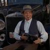 Frame from 1967 trailer for Bonnie and Clyde showing Warren Beatty sitting on a car bumper displaying a Tommy gun