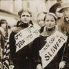 Two girls wearing banners with slogan 'ABOLISH CHILD SLAVERY!!' in English and Yiddish, one carrying American flag. Probably taken during May 1, 1909 labor parade in New York City.