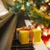 Yellow present lays on the keys of a piano with Christmas tree in the background