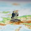 Two miniature figurines of businessmen shaking hands standing on a Euro coin on a map of Europe.