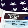 A piece of paper that reads 'United States Census 2020' with a blue pen and an American flag in the background