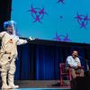 a woman stands on stage in an astronaut like suit. next to her sit two scientists with mics, talking to ira flatow