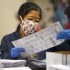 A election worker wearing a mask looks at a ballot.