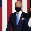 biden and harris, wearing masks, walking on stage, with an american flag in the background