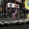 People walk by sand bags in front of a building in Times Square as Hurricane Sandy arrives