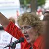  Christa Brown, a woman with glasses, short blond hair and red shirt, speaks into a microphone and raises her fist at a rally in Birmingham, Ala. outside the 2019 SBC annual meeting.