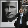 A man enjoys a drink as he walks past a portrait of Russian President Vladimir Putin displayed among portraits of Russian athletes, winners of the Sochi 2014 Winter Olympics at the photo exhibition.