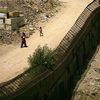 People walk past each other on opposite sides of the fence along the U.S. Mexican border