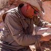 a man sits next to sandstone and brushes away dirt with a brush