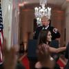 President Donald Trump watches as a White House aide reaches to take away a microphone from CNN journalist Jim Acosta during a news conference in the East Room of the White House