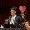 a man in a top hat holds an award made of a cutout heart with a stethoscope around it, that reads 'ig nobel'