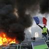 A demonstrator waves the French flag onto a burning barricade on the Champs-Elysees avenue with the Arc de Triomphe in background, during a demonstration 