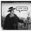 An old photograph of a woman next to a fluffy cat on a pedestal. Speech bubble for the woman says 'I LOVE YOU!' The cat says 'FINE.'
