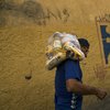With a mural depicting the eyes of Veneuzela's late President Hugo Chavez, Carlos Gonzales carries a bag with food delivered by the government for the poorest people in the Antimano neighborhood 