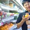 a smiling dad hands his infant an orange in a grocery store