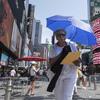 A woman uses an umbrella to block out the sun while walking through Times Square.