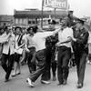 Sam Mitchell, a 46-year-old black janitor, is assaulted by George Miller as police escort Mitchell after he was shot in the stomach during rioting in the edge of the downtown area of Detroit, Mich., J