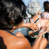 three women sitting lined up putting sunscreen on each other's backs on the beach