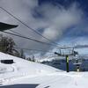 a ski lift going downards on a mountain overlooking a pristine lake. the mountain sides are snowy