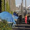 In this May 7, 2018 file photo, tents used by homeless people are shown on either side of a sidewalk in Seattle with CenturyLink and Safeco Fields in the background. 