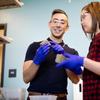 a man with gloves and lab goggles smiles while looking at a block of san with a female student