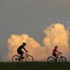 People ride bikes with cumulus clouds in the background, on the Mississippi River levee in Jefferson Parish, a suburb of New Orleans, Tuesday, July 14, 2020.