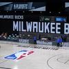 Officials stand beside an empty court at the scheduled start of an NBA basketball first round playoff game between the Milwaukee Bucks and the Orlando Magic, Wednesday, Aug. 26, 2020, in Florida.