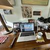 A home office desk cluttered with statues, photos and a wire shelf. 