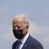 Joe Biden wears a black face mask and a navy suit. He looks into the distance, with blue sky in the background.