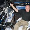 a white bald astronaut in a black shirt and cargo pants floats in zero gravity inside a space craft that looks out over the earth
