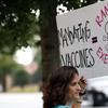 Woman holds sign which reads 'MANDATING VACCINE = RANDOM EXECUTIONS' with a skull and crossbones.