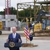 Biden stands in front of a construction site with a frame of a building behind him.