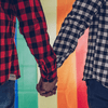 Two men hold hands in front of a PRIDE flag