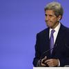 John Kerry, United States Special Presidential Envoy for Climate grimaces behind a lectern in front a blue background.