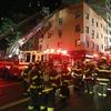 Firefighters and firetrucks with ladders surround a four story building at night