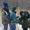 four people in jackets in a snowy field using binoculars to look up at birds
