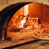 two pizzas in a traditional pizza oven with fire burning behind it