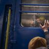 A child and adult wave goodbye through the window of a train in Ukraine painted yellow and blue.