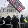 Police in front of the US capitol hold barriers with smoke around them. Behind them is a flag that's only partially in the show, with the word 'protected' on it.