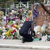 A man kneels in front of the brick Robb Elementary School sign that's covered in flowers and tributes. 