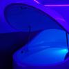 A sensory deprivation tank with the lid open, lit up by a blue light.