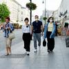 six white people walking on a european street. four people are walking towards the camera, two of which are wearing masks, and the two people not facing the camera walking away, appearing to not be we