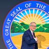 Ohio Governor Mike DeWine stands on a stage in a suit in front of the state seal of Ohio