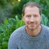 Portrait of Andrew Sean Greer, man wearing a sweater in front of green leaves