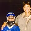 Rachel Matlow as a kid, wearing a royal blue hockey uniform with a helmet labeled 'RACHEL', standing next to their mom, Elaine Mitchell. Elaine has her arm around Rachel. They're both smiling.