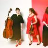 Four women holding musical instruments, standing against a white and red background.