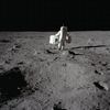 Buzz Aldrin in his astronaut suit can be seen walking on the surface on the moon with a pitch black space in from of him.